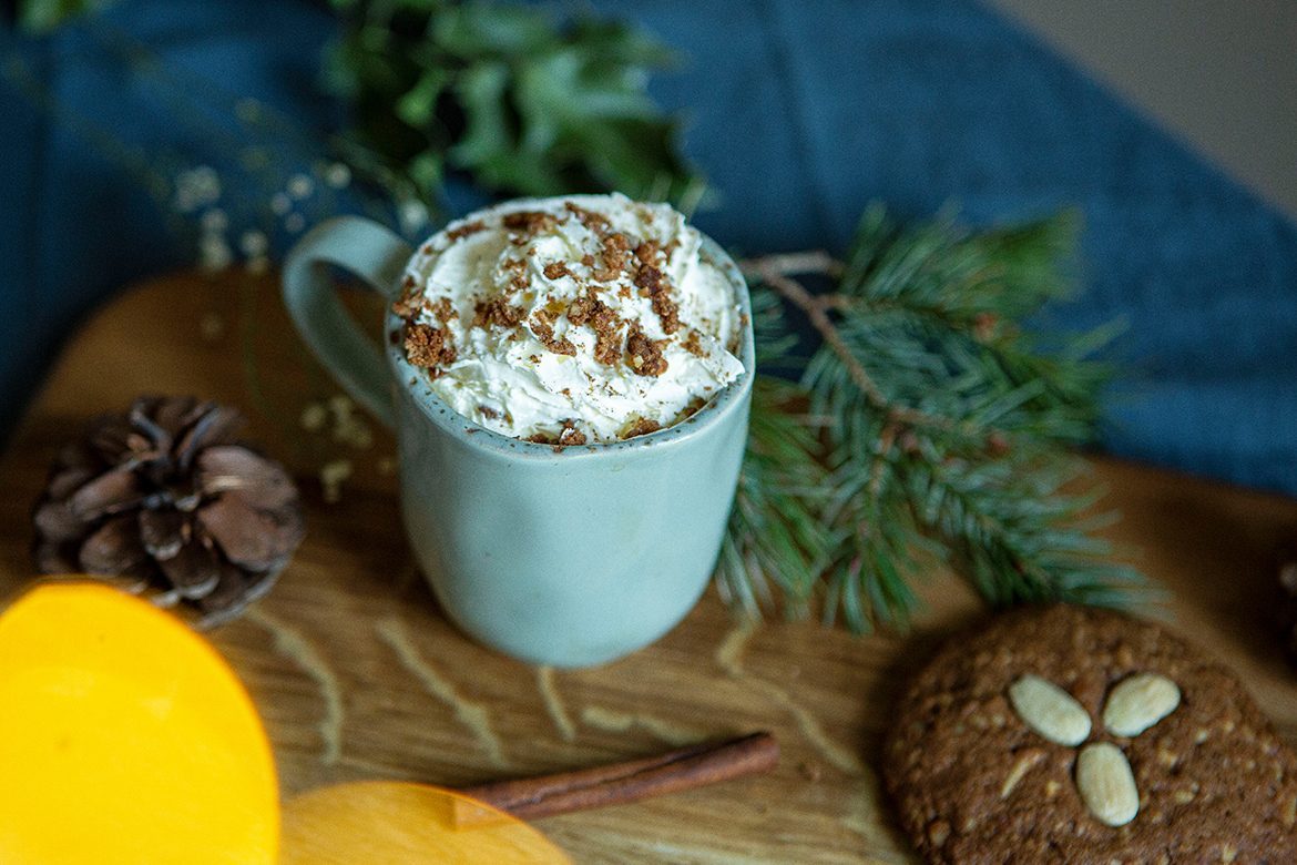 Der selbst gemachte Lebkuchen-Latte ist mit Sahne dekoriert und steht auf einem Brettchen, auf dem ein Lebkuchen liegt.