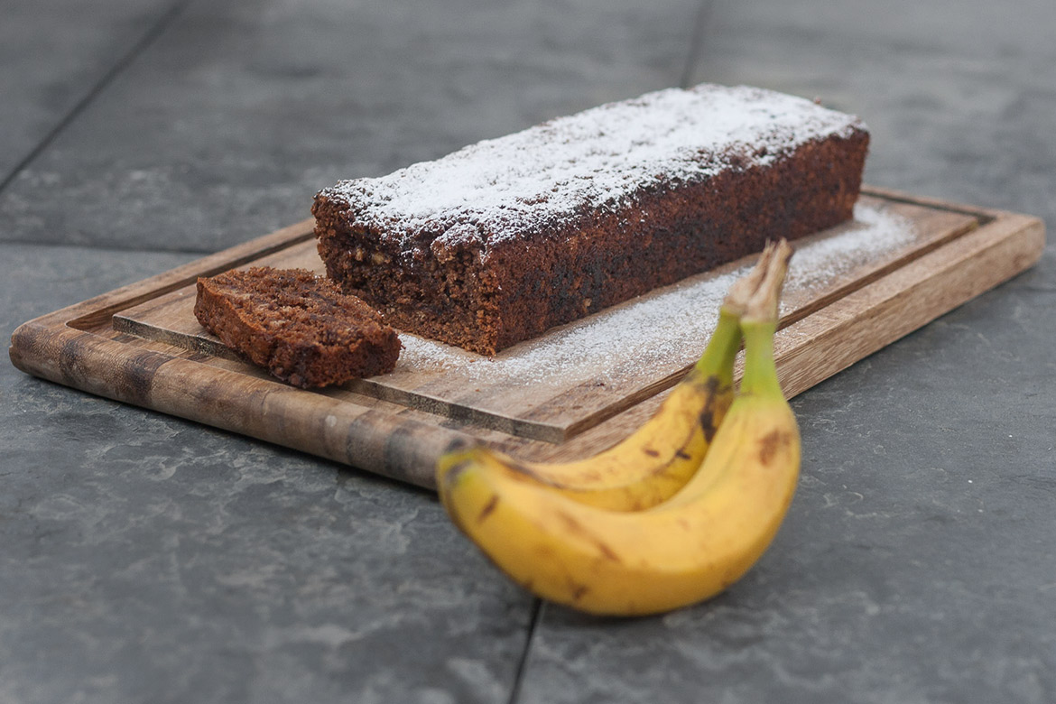 Veganes Bananenbrot liegt angeschnitten auf einem Schneidebrett.