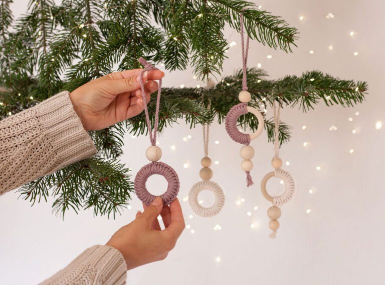 Der Makramee-Baumschmuck wird von einer Hand in einen Tannenzweig gehängt.