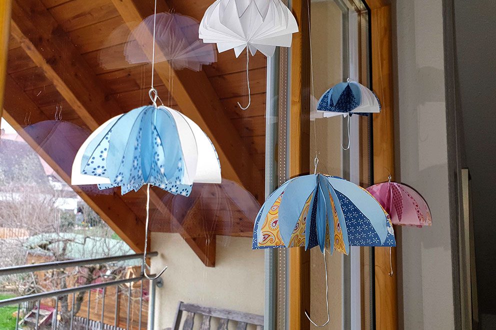 Die bunten Regenschirme aus Papier hängen vor einem Fenster.