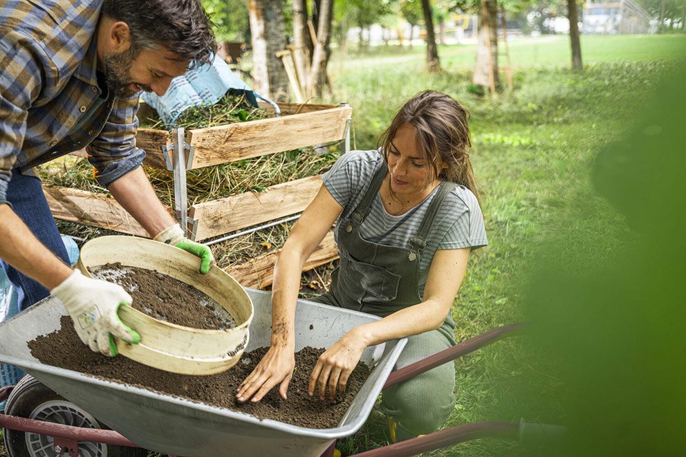 Eine Frau und ein Mann mischen und sieben die Gartenerde in einer Schubkarre.