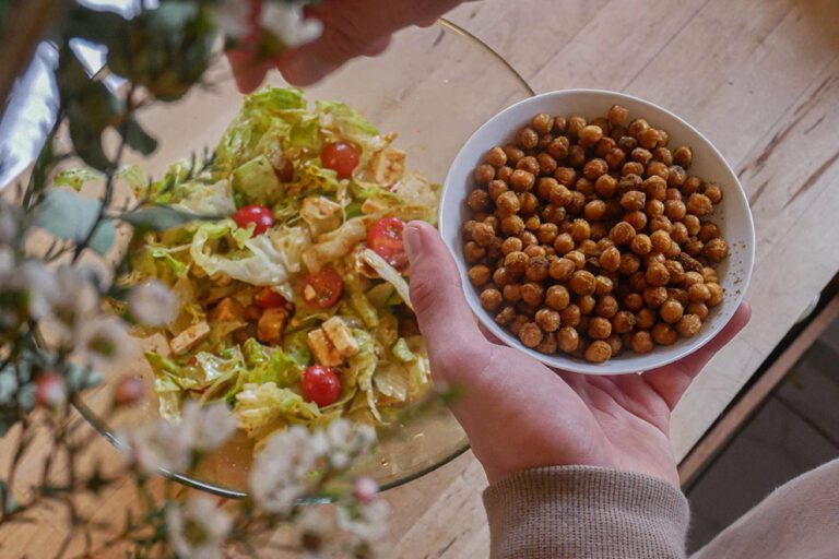 Die gerösteten Kicherebsen werden aus einem kleinem Schälchen über den Salat gestreut.