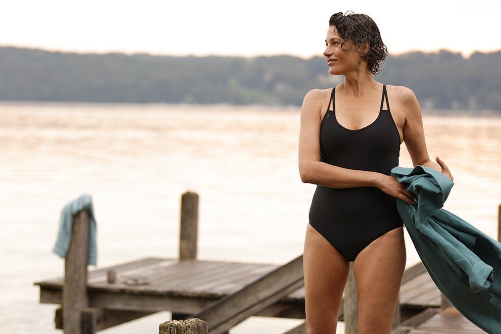 Eine Frau in einem dunklen Badeanzug kommt vom Baden im See zurück.