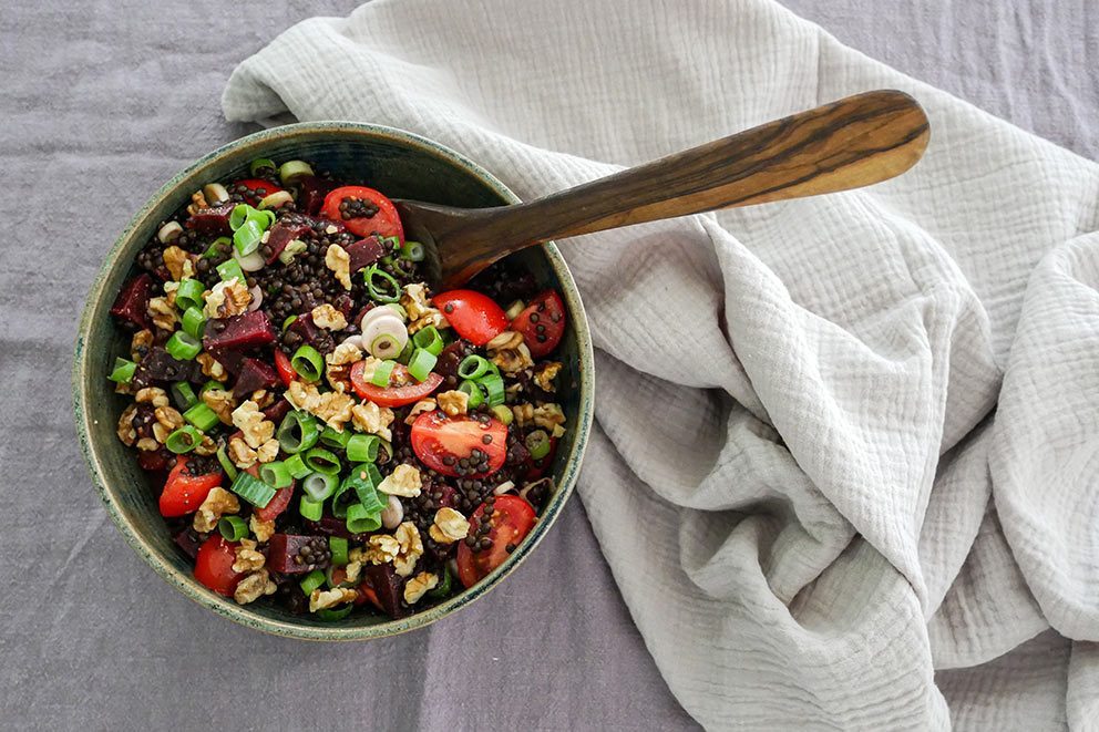 Eine Schüssel mit Linsensalat steckt auf einem mit Stoff überzogenem Tisch.