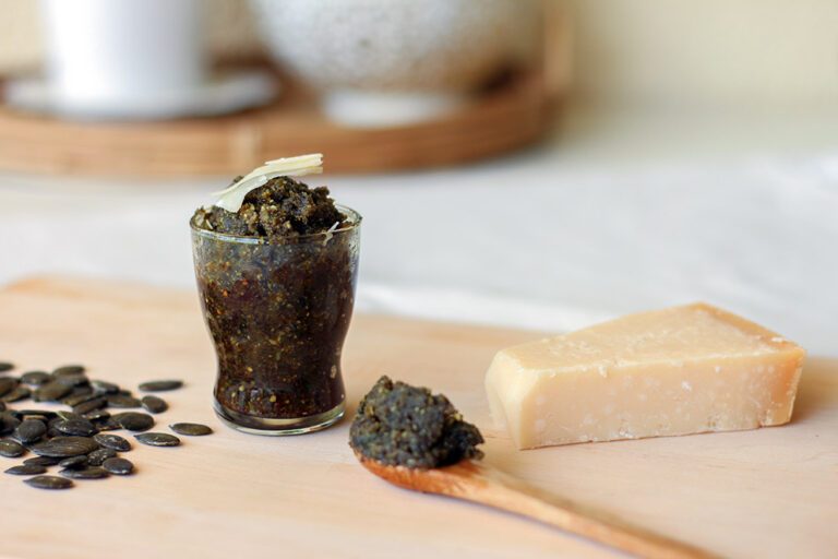 Das selbst gemachte Kürbiskern-Pesto steht in einem kleinen Glas auf einem Holzbrett auf dem Tisch.