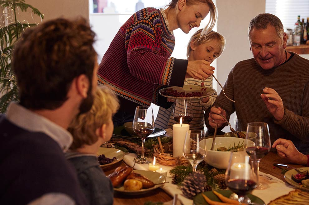 Eine Familie genießt das Weihnachtsmenü, die Mutter schöpft ihrem Sohn Essen auf den Teller.