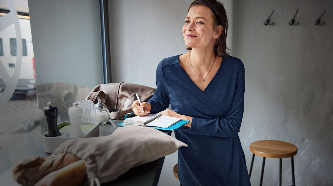 Frau in Bio-Wollkleid sitzt in einem Café und schreibt in ein Notizbuch