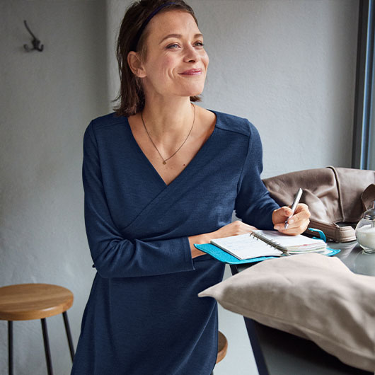 Frau in einem kuschligen Bio-Kleid schreibt Notizen in einem  Café