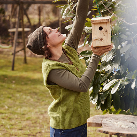 Frau hängt nachhaltigen Nistkasten im Garten auf an einem Baum