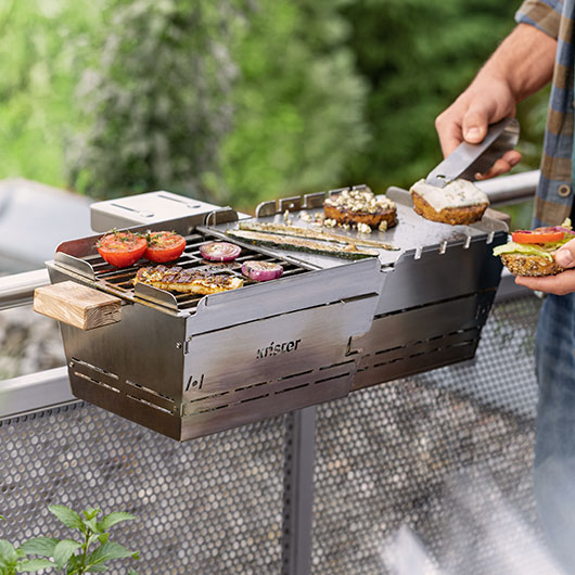 Nachhaltiger Edelstahl Grill mit Grillgut, am Balkon befestigt