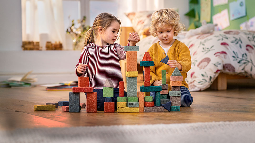 Kinder spielen mit bunten Bauklötzen aus Kork in einem gemütlichen Kinderzimmer