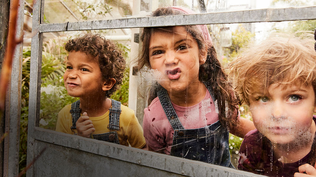 Kinder in Bio-Mode von Waschbär schneiden Grimassen hinter einer Gewächshausscheibe.