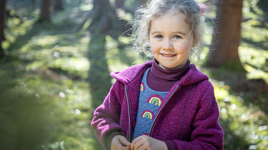 Mädchen im Wald in kuscheliger und nachhaltiger Bio-Wollwalk-Kleidung
