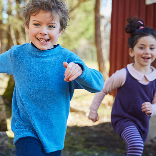 Junge und Mädchen in farbenfrohem und gemütlichem Pullover und Cardigan spielen im Wald