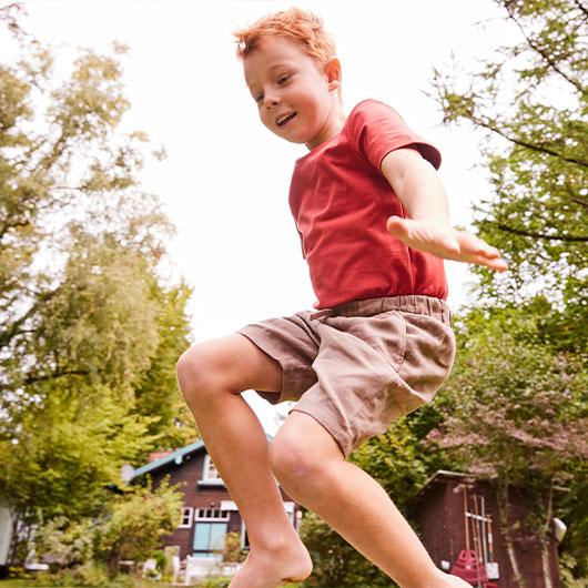 Springender Junge in rotem Shirt und taupe-farbener kurzer Hose von Waschbär