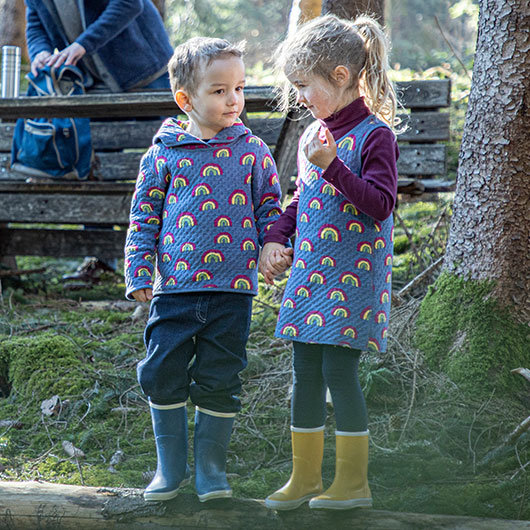 Junge und Mädchen in Regenbogen Wende-Kleidung beim Waldspaziergang