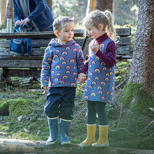 Junge und Mädchen in Regenbogen Wende-Kleidung beim Waldspaziergang
