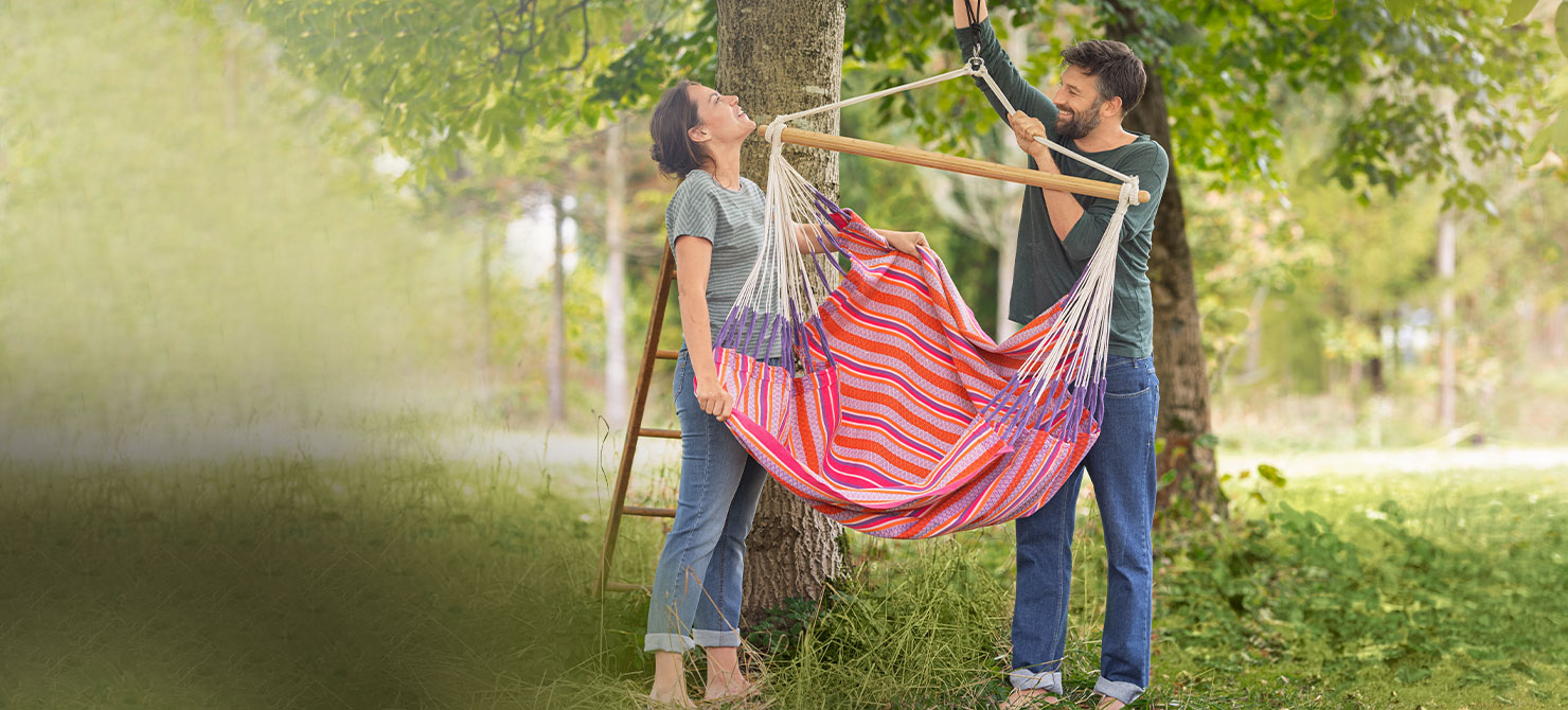Frau und Mann befestigen Hängesessel in einem Baum im Naturgarten